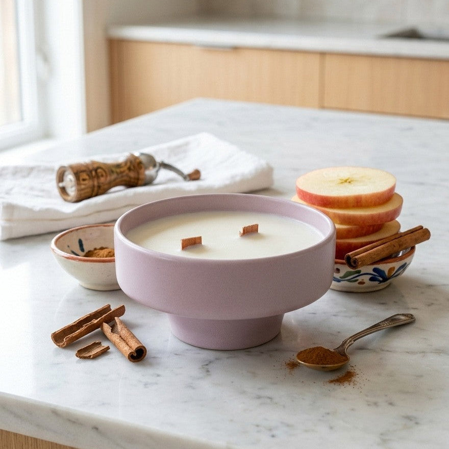 PRESENTE Taller Artesanal pastel pink ceramic double wick candle with pedestal base, wood wicks, on marble counter with cinnamon sticks and apple slices.