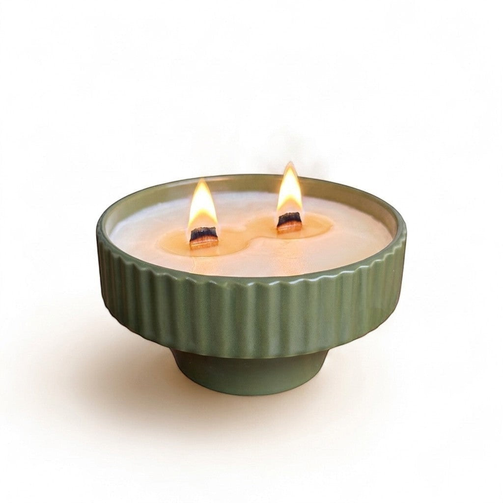 PRESENTA Vela de cerámica acanalada de color verde salvia de Taller Artesanal con dos mechas de madera encendidas.